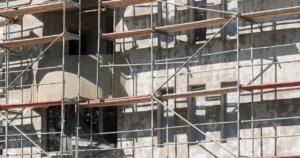 Andamio tubular de acero con plataformas de madera sobre la fachada de un edificio en construcción con paredes de estuco
