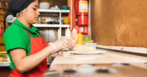 Trabajadora de cocina con guantes y delantal rojo preparando comida en un restaurante
